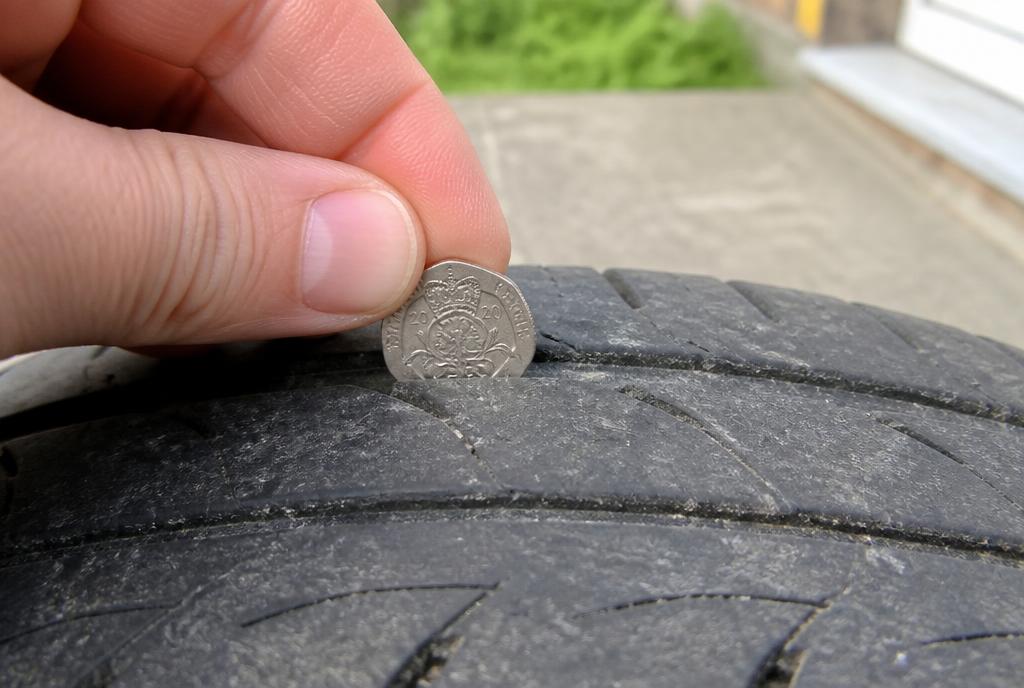 A twenty pence coin held in the tread groove of a tyre for a depth check